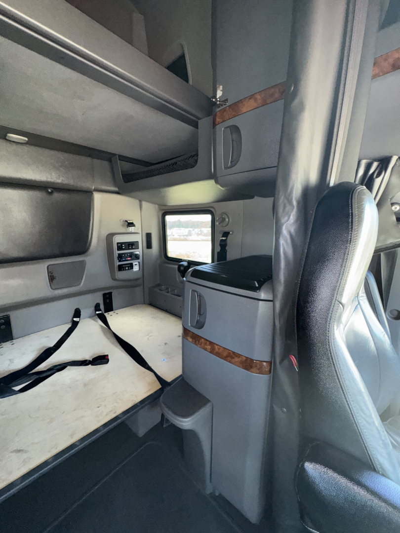 Interior sleeper cab of a 2019 International LT625 truck showing bunk area, storage cabinets, and captain seat with window view.