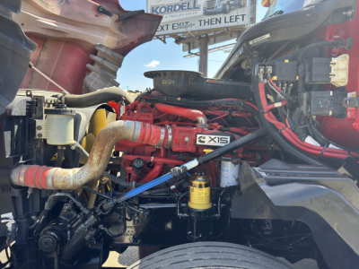 Engine bay of a 2019 International LT625 truck showing red engine components, hoses, and a yellow filter. Visible labels include X15 badge and various hoses and wiring.