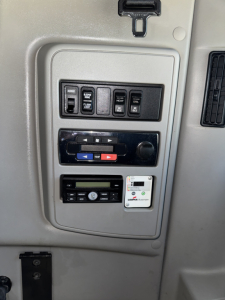 Dashboard panel with multiple switches and gauges in a truck cab showing labeled controls for A/C, heat, defrost, joystick-like rocker switches, a radio, and control labels.