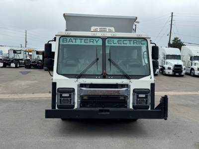 Mack LR64 BE front view showing large black front bumper, two square headlights, windshield wipers, and 'BATTERY ELECTRIC' text on the windshield. Front grille with 'MAC K' badge in center.
