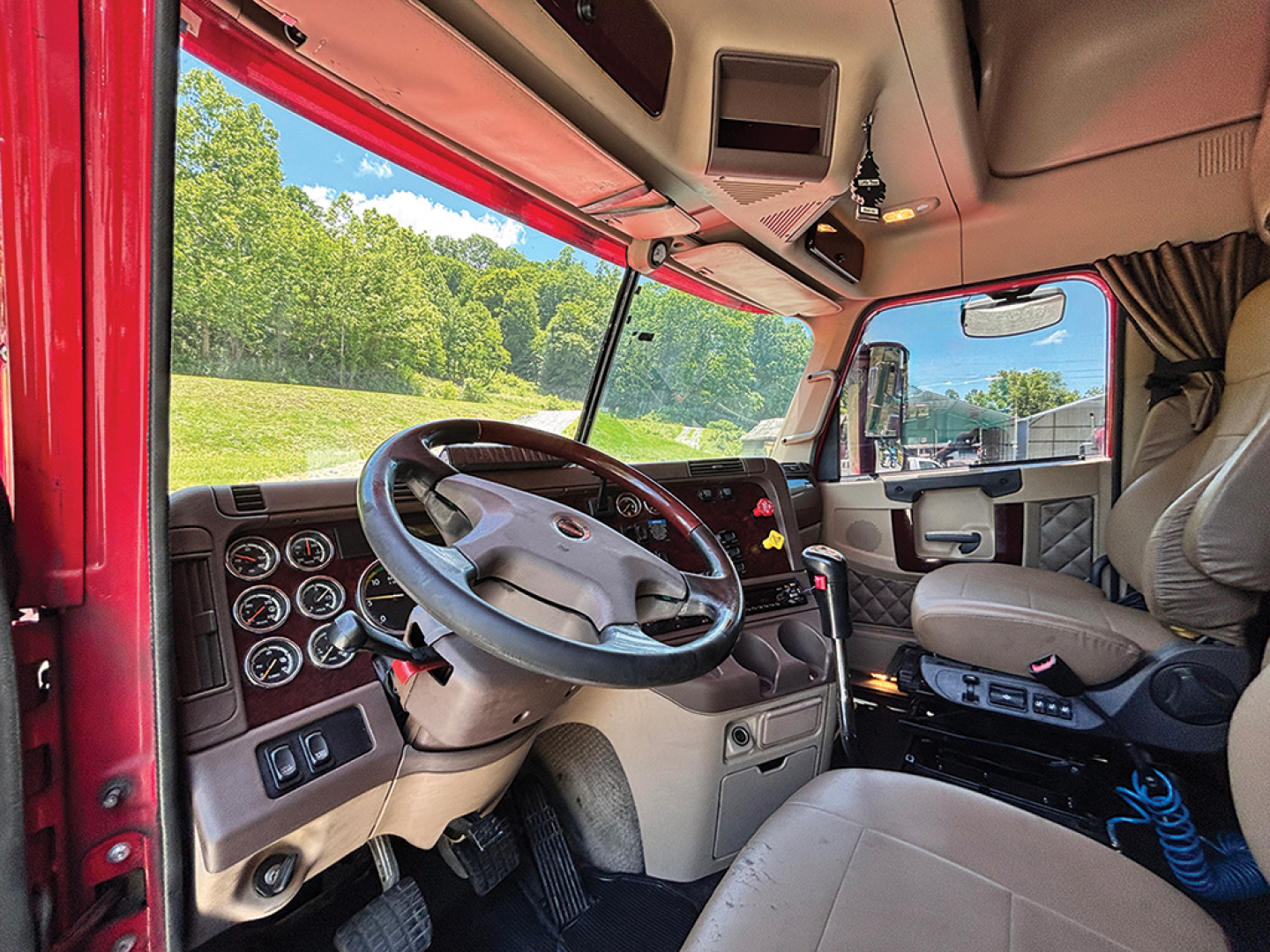 Interior of a Freightliner Coronado truck cabin with steering wheel, dashboard, and beige seats visible through the open door