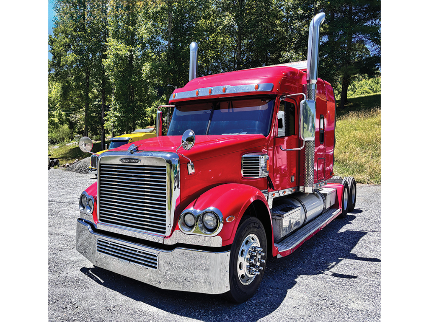 Red Freightliner Coronado heavy-duty truck, day sun, chrome grille, dual exhaust stacks, sleeper cab, chrome bumper, large front wheels.