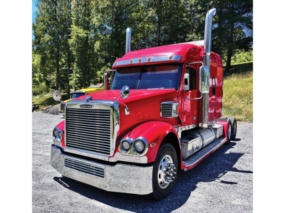 Red Freightliner Coronado heavy-duty truck, day sun, chrome grille, dual exhaust stacks, sleeper cab, chrome bumper, large front wheels.