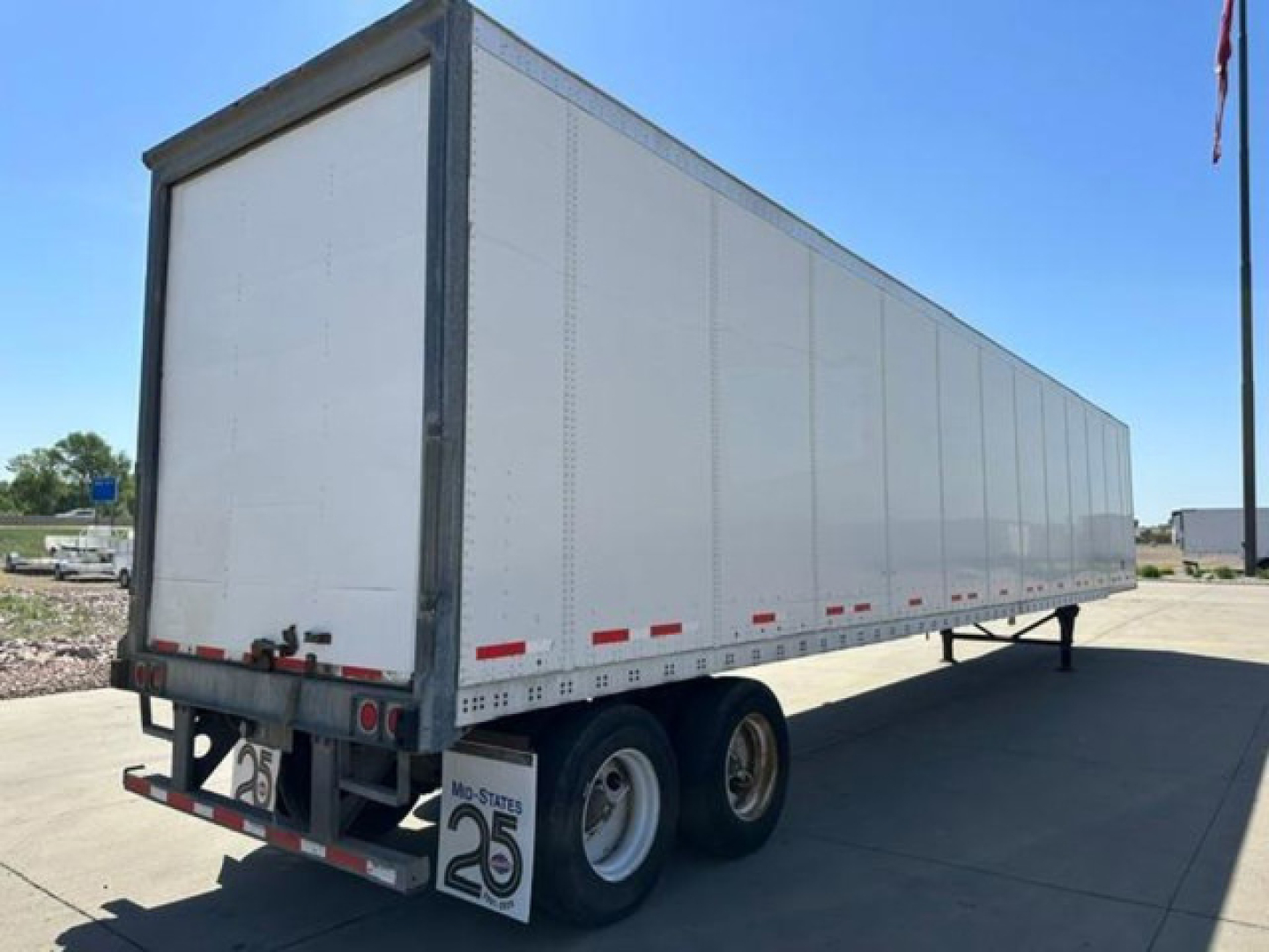 Flatbed trailer showing white exterior with dual rear axles, rear bumper with license plates, and red reflectors along lower side. Visible text includes stock number U90806 and trailer markings.