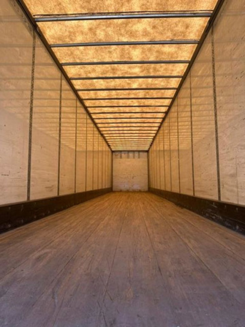 Trailer interior showing empty cargo space with wooden floor and side walls, long rectangular trailer leading to rear door.