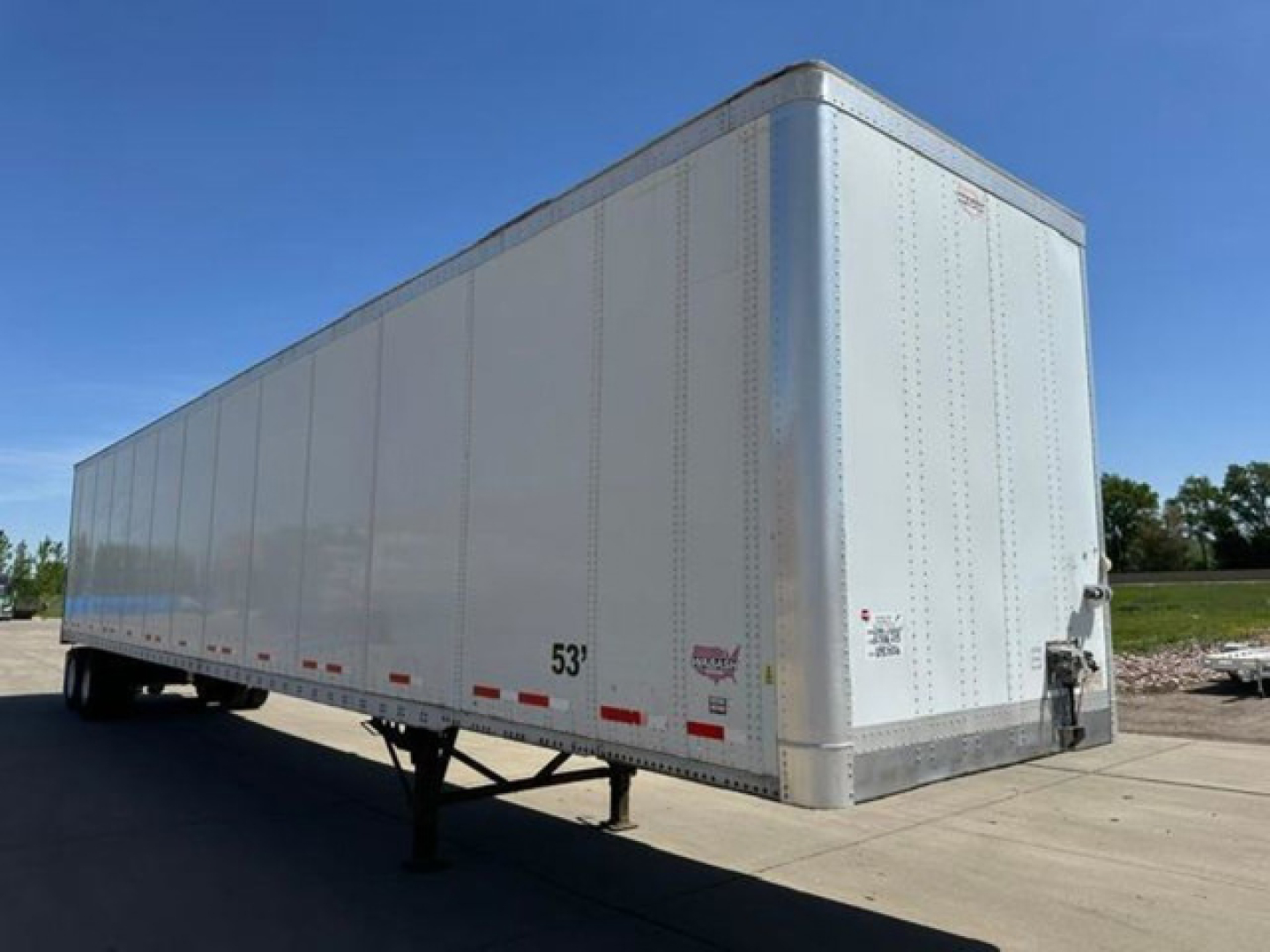 Trailer side view showing a white 53' Wabash van trailer with front corner, visibility of wheels and landing gear, and small markings near the rear. Text on side includes '53'' and small decals.