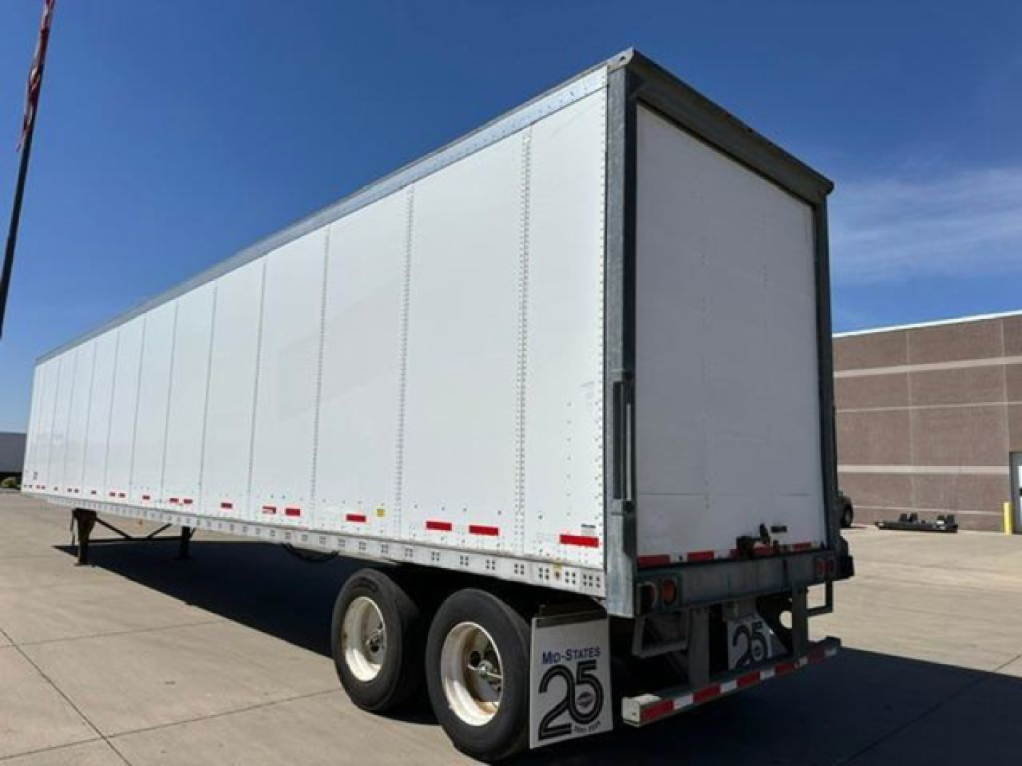Trailer side view showing a white Wabash van trailer with two rear dual axles and a closed rear door.