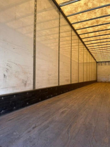 Interior of a loading trailer showing wooden floor and white walls with ribbed metal frame, long empty cargo space.