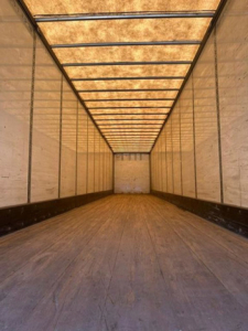 Trailer interior showing empty cargo space with wooden floor and side walls, long rectangular trailer leading to rear door.