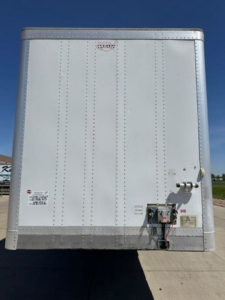 Rear view of a white Wabash trailer: riveted panels, hitch/tongue area with electrical connector, safety chains, and labeling stickers.
