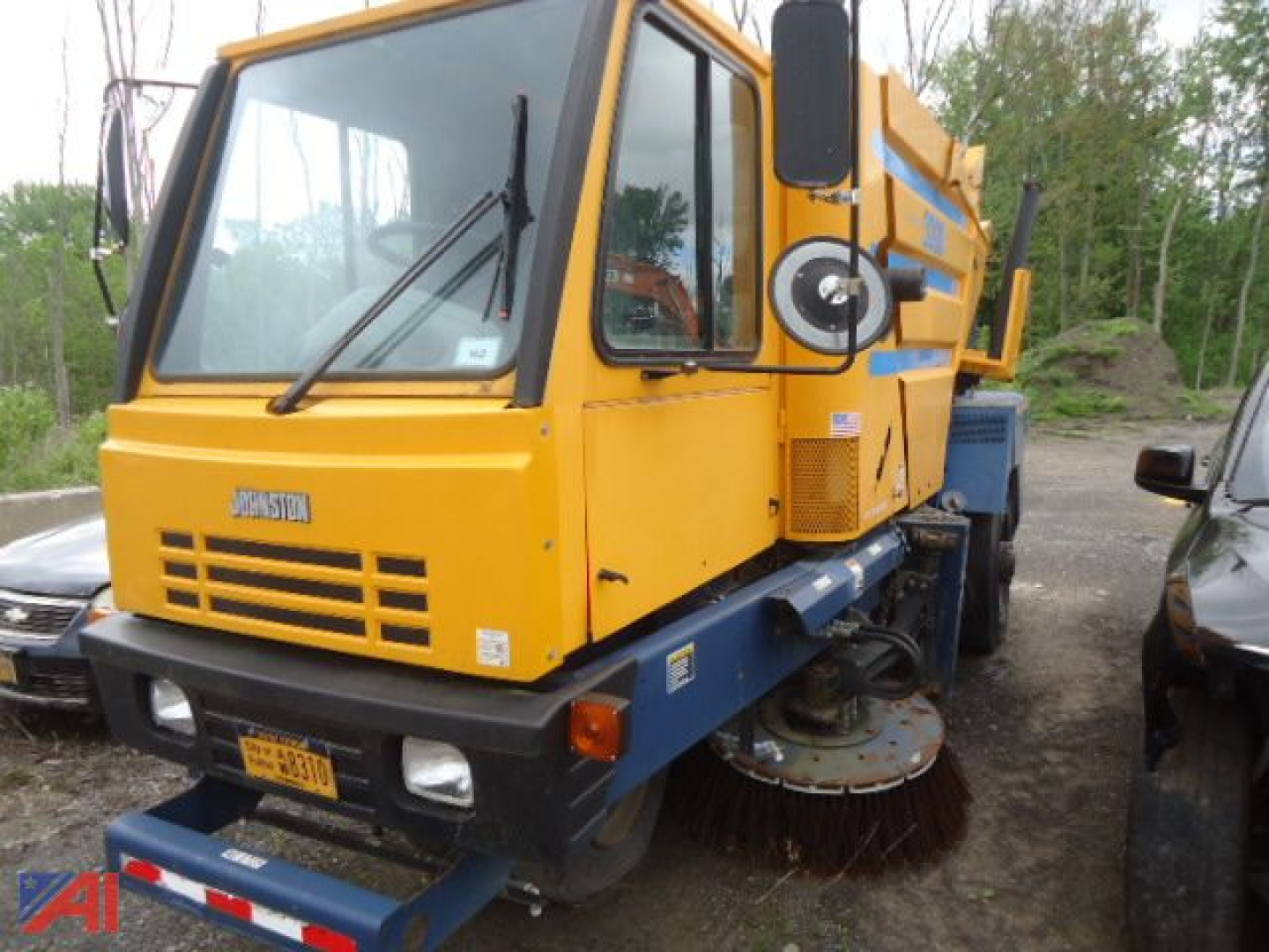 Johnston 3000 road sweeper truck in yellow and blue, front-left view with side brush and rear containment, black text on grille.