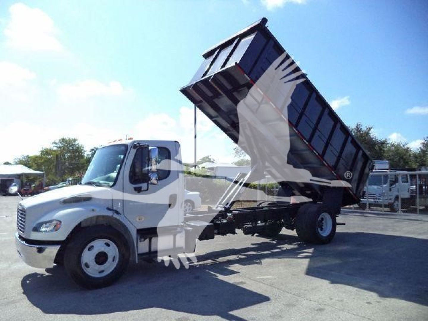 Dump truck in service bay showing raised dump bed on Freightliner M2 106 with white cab and black bed
