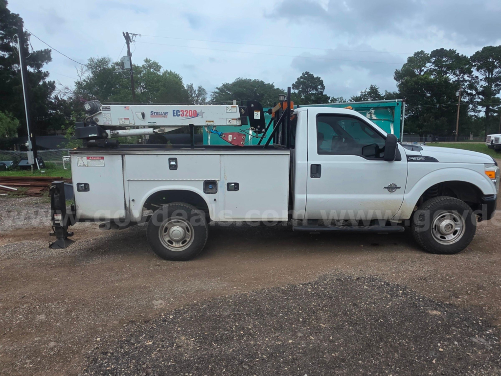 Side view of a white Ford F-350 service truck with utility bed and crane equipment in a yard.