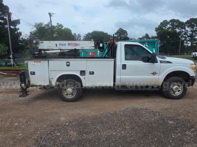 Side view of a white Ford F-350 service truck with utility bed and crane equipment in a yard.