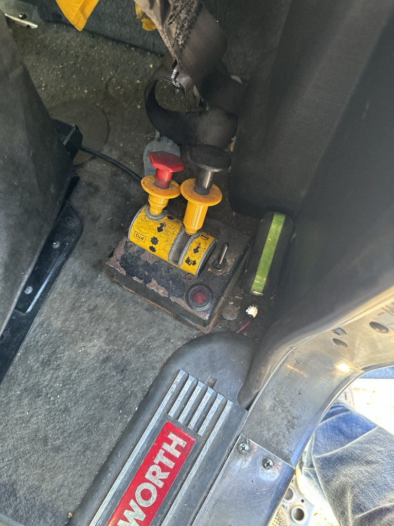 Vehicle interior showing hydraulic controls with multicolored levers and safety switch near floor of cab and starter block.