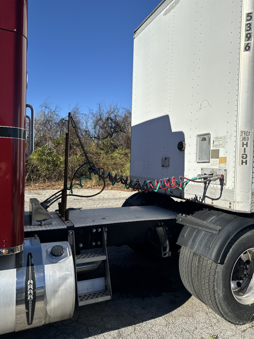 Rear side of a 2014 Kenworth T660 tractor showing sleeper cab, fuel tank, and wheel with fender; air/electrical lines and air hoses near the trailer coupling.
