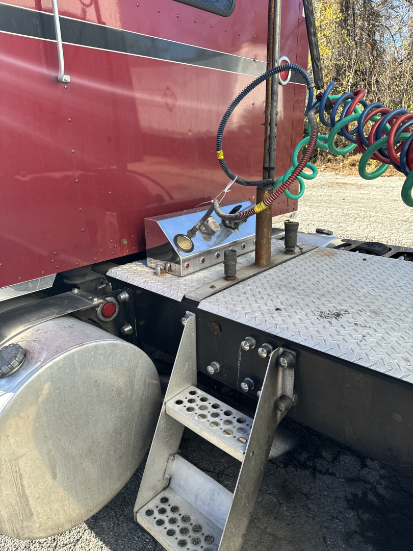 Kenworth T660 cab area showing metal steps and air/electrical lines along side, diesel fuel tank, metal diamond plate platform; visible hoses and connectors near sleeper cab.