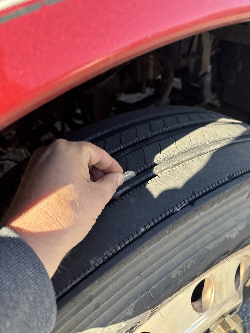 Tire tread close-up on Kenworth T660 wheel well with a hand pressing the tire sidewall.