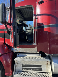 Truck cab door open of red 2014 Kenworth T660 showing entry step, the driver seat, and interior dashboard area.