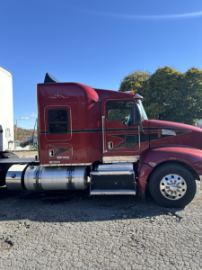 Kenworth T660 sleeper cab truck in red with chrome fuel tanks and steps visible, side view showing cab window and door panel, VIN not visible
