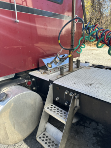 Kenworth T660 cab area showing metal steps and air/electrical lines along side, diesel fuel tank, metal diamond plate platform; visible hoses and connectors near sleeper cab.
