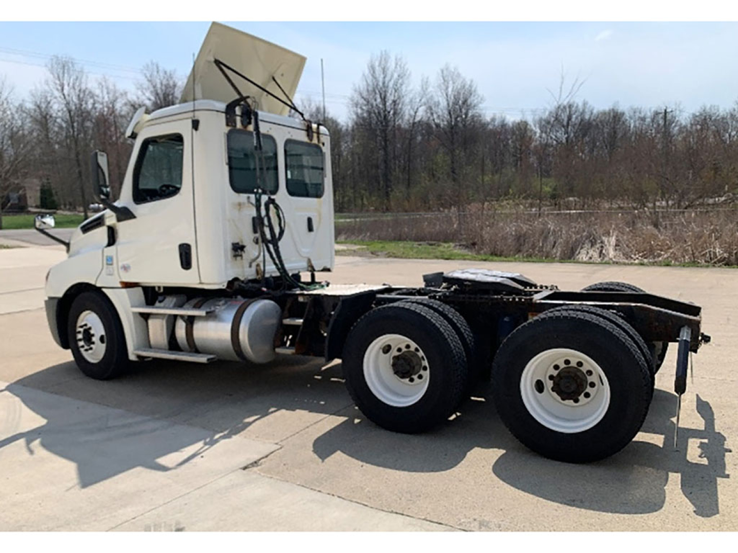 Side view of a 2019 Freightliner Cascadia126 daycab tractor with dual rear axles and exposed chassis, white cab, large fuel tanks, and sturdy wheels.