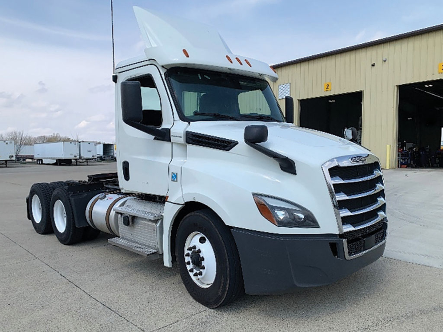 Truck in a yard: white 2019 Freightliner Cascadia126 daycab tractor with dual rear axles, fuel tank, and chrome grille. No visible text other than generic truck parts.