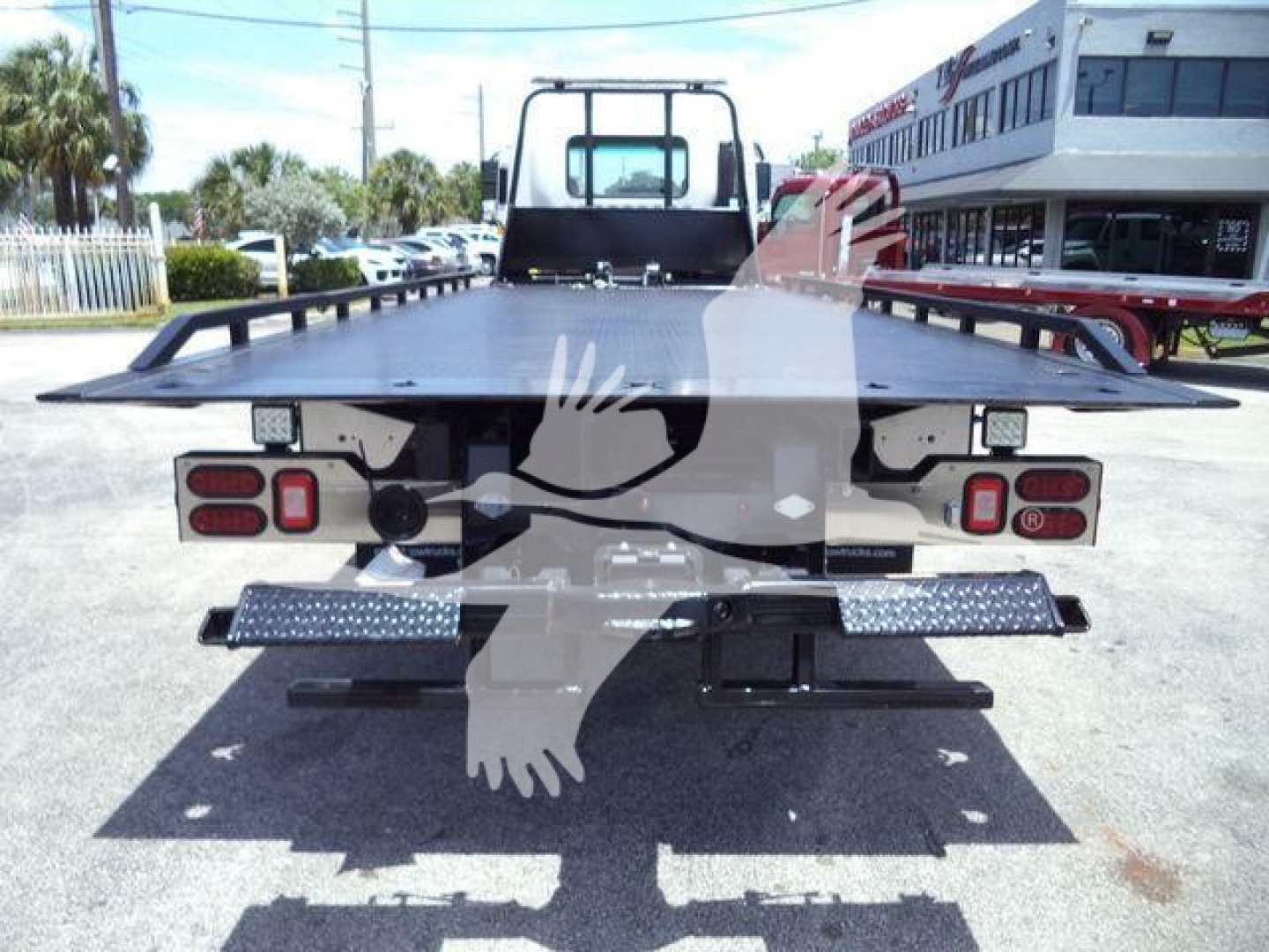 Flatbed tow truck rear view showing tail lights and bumper platform on a new 2024 Isuzu FTR.