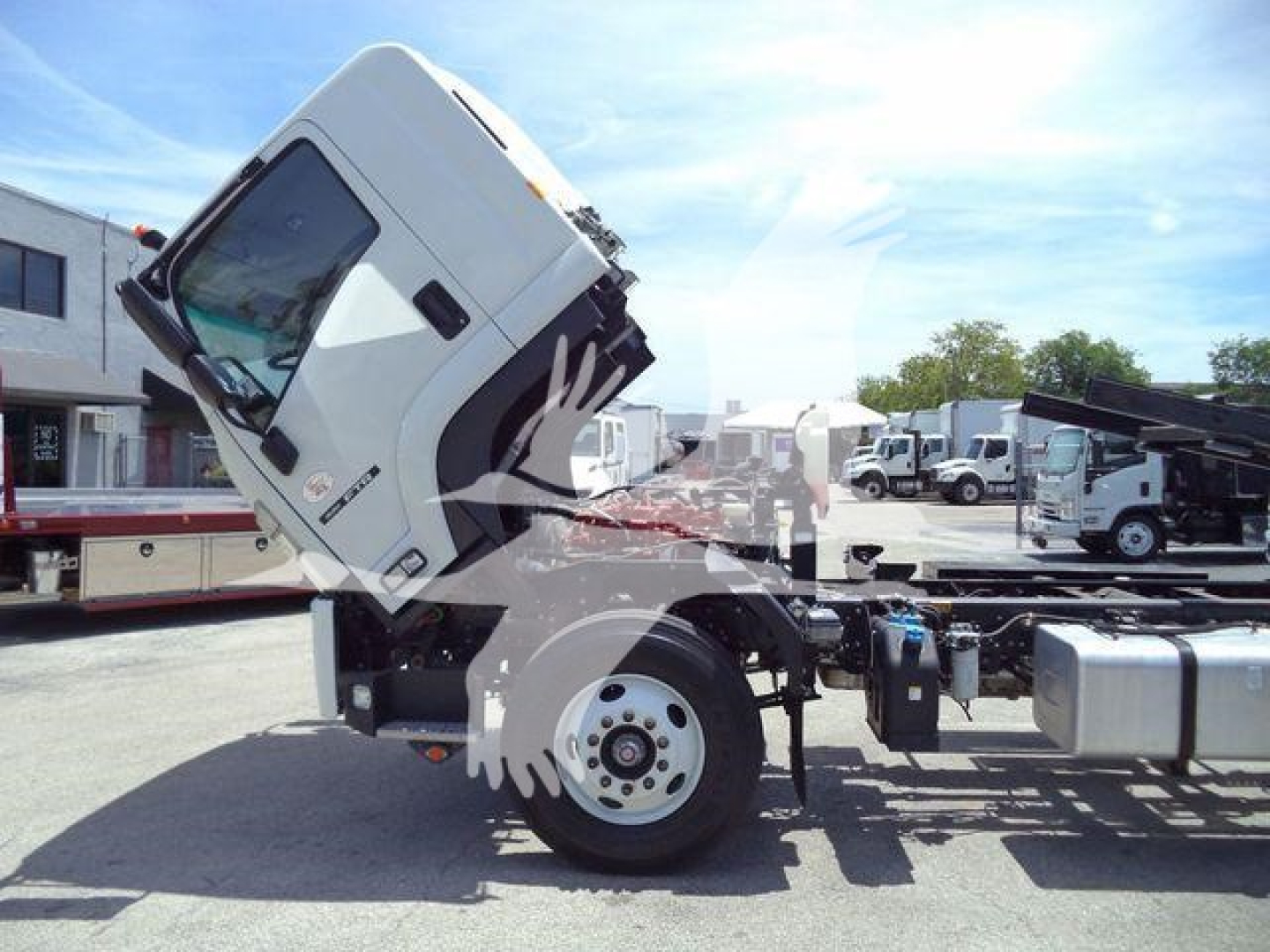 Isuzu FTR truck cab tilted upward on a roll-off tow chassis, showing front wheel and cab side with Isuzu emblem.