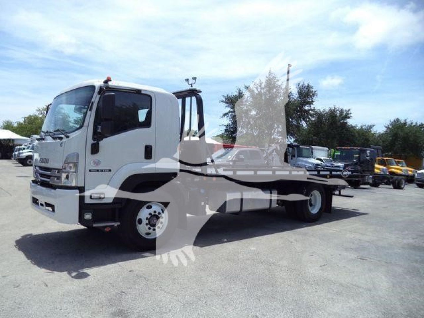 Isuzu FTR tow truck chassis with flatbed, white cab, side view showing wheel, clear windshield, and equipment yard in background.