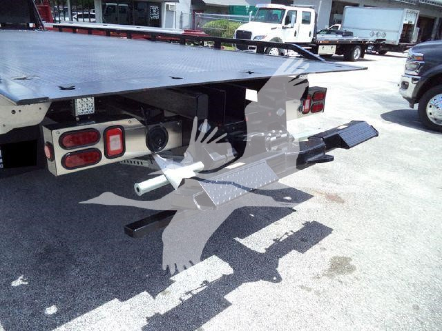 Isuzu flatbed tow truck rear with platform and rear outriggers visible, tail lights, and towing apparatus in view.