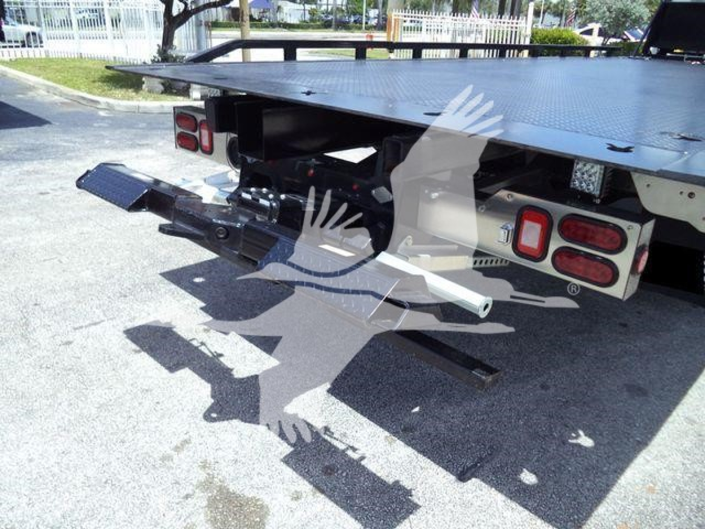 Isuzu flatbed tow truck rear view showing hydraulic hitch and taillights with platform edge and support arms.