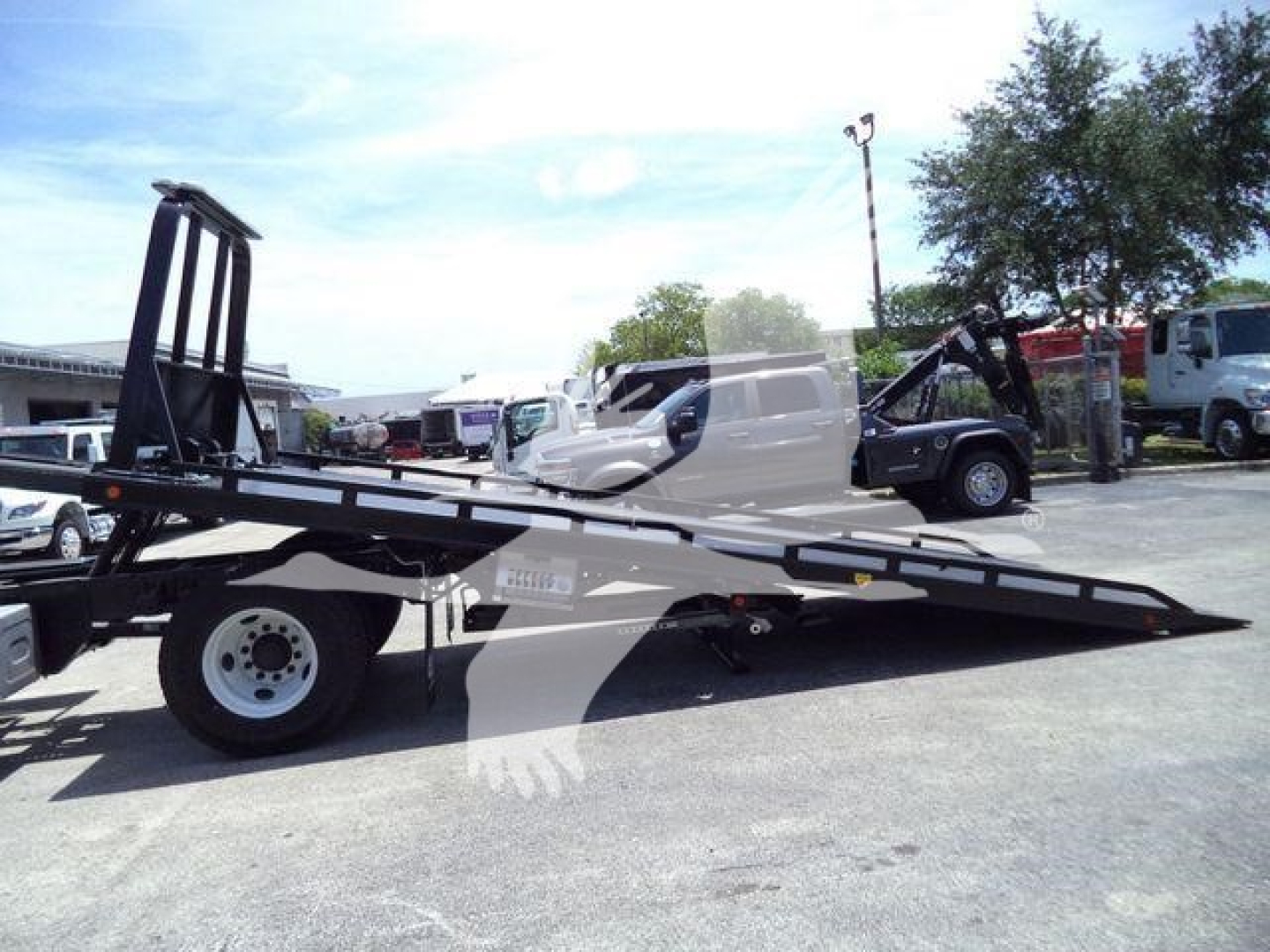 Isuzu tow truck with flatbed and wheel in foreground; visible text on side reads models and vehicle components.