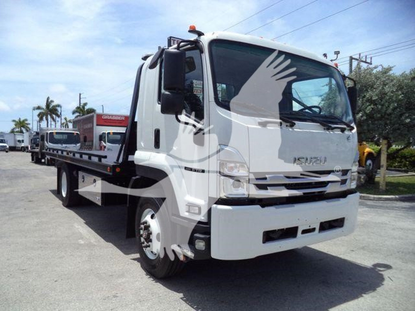 Isuzu forward-control tow truck with flatbed, white cab, visible cab door and windshield. Nozzle/branding text on grille area, possibly Isuzu emblem; truck body hardware and cabside mirror visible; no legible model text clearly readable.