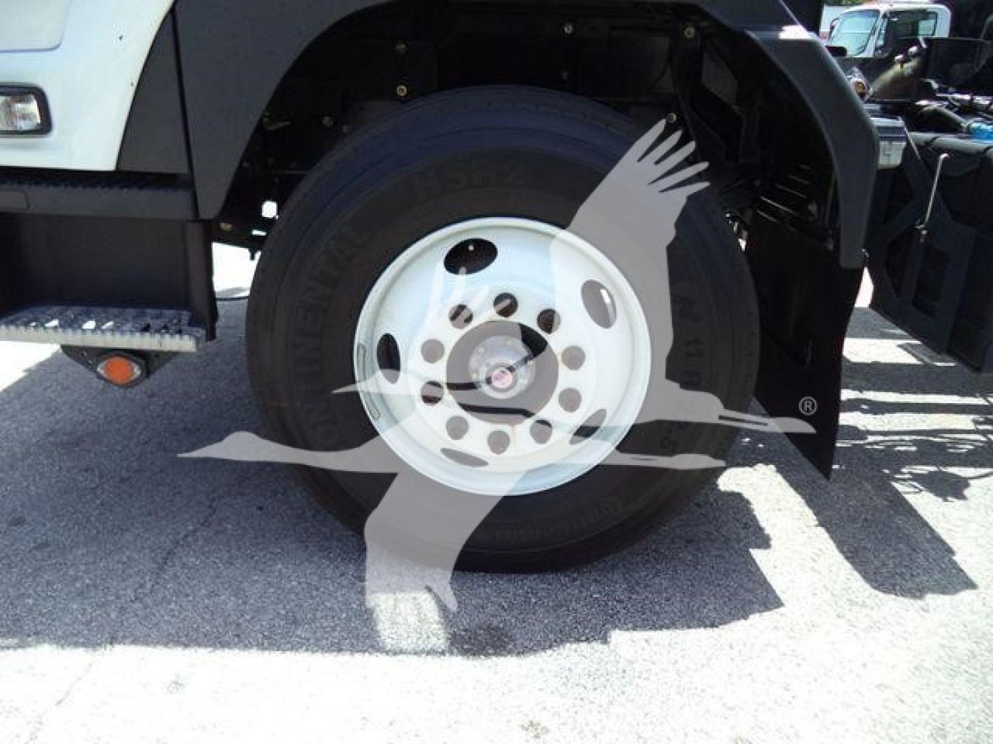 Isuzu truck front wheel and tire shown in side view with white wheel and black tire, wheel well and step bumper visible.