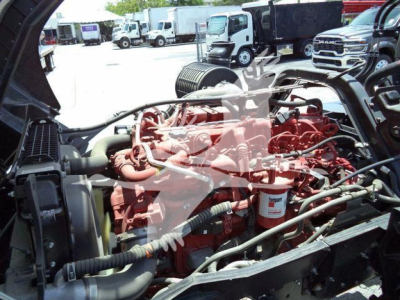Isuzu engine bay with red engine and various hoses and components visible under open hood in a truck showroom lot.