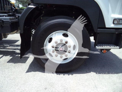 Isuzu truck front wheel showing steel hub, tire, and fender; part of a rollback truck in a dealership lot.