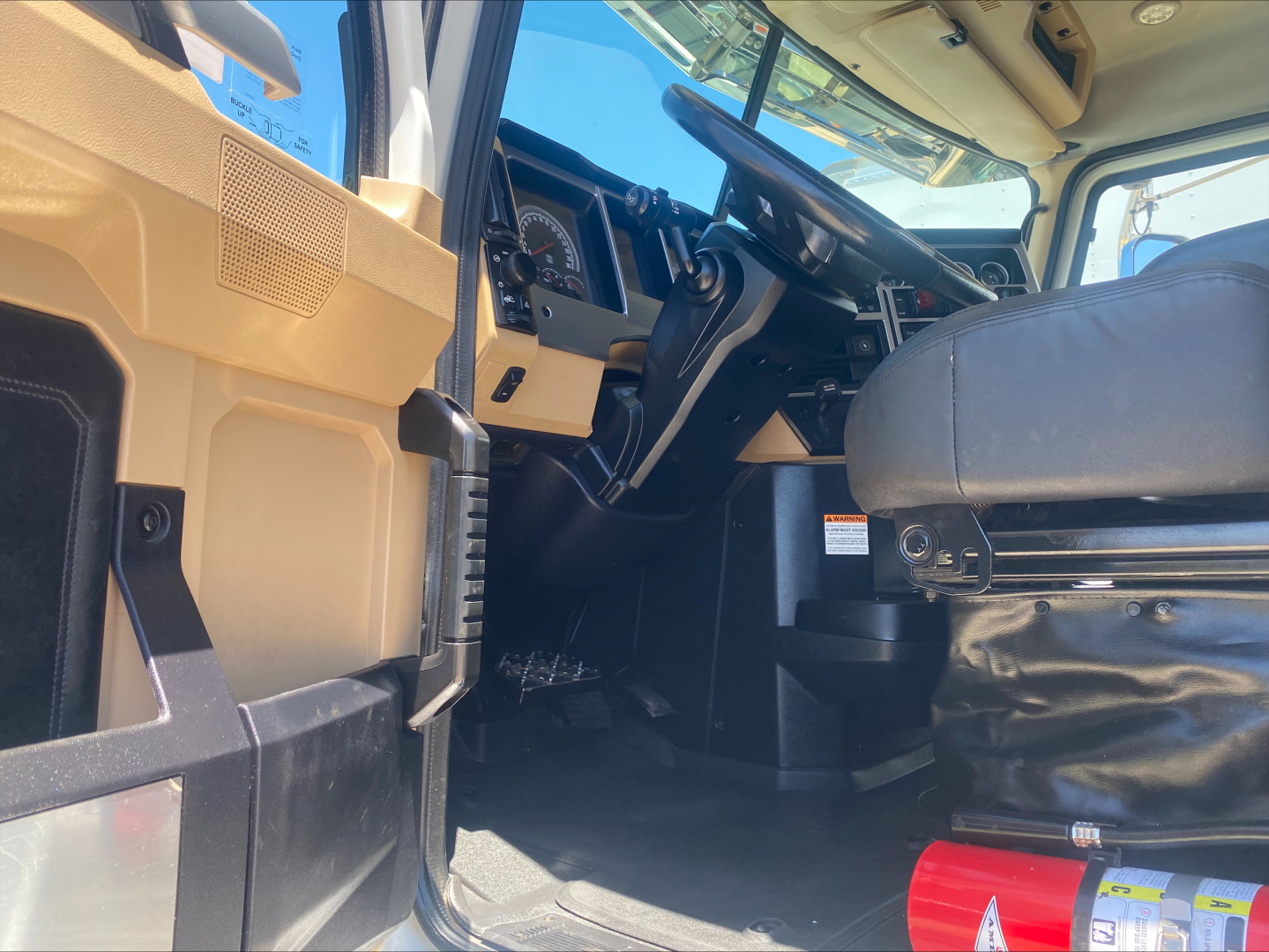Truck cab interior of a 2024 Mack PI64T with steering column, dashboard, and seat visible; beige and black plastic panels.