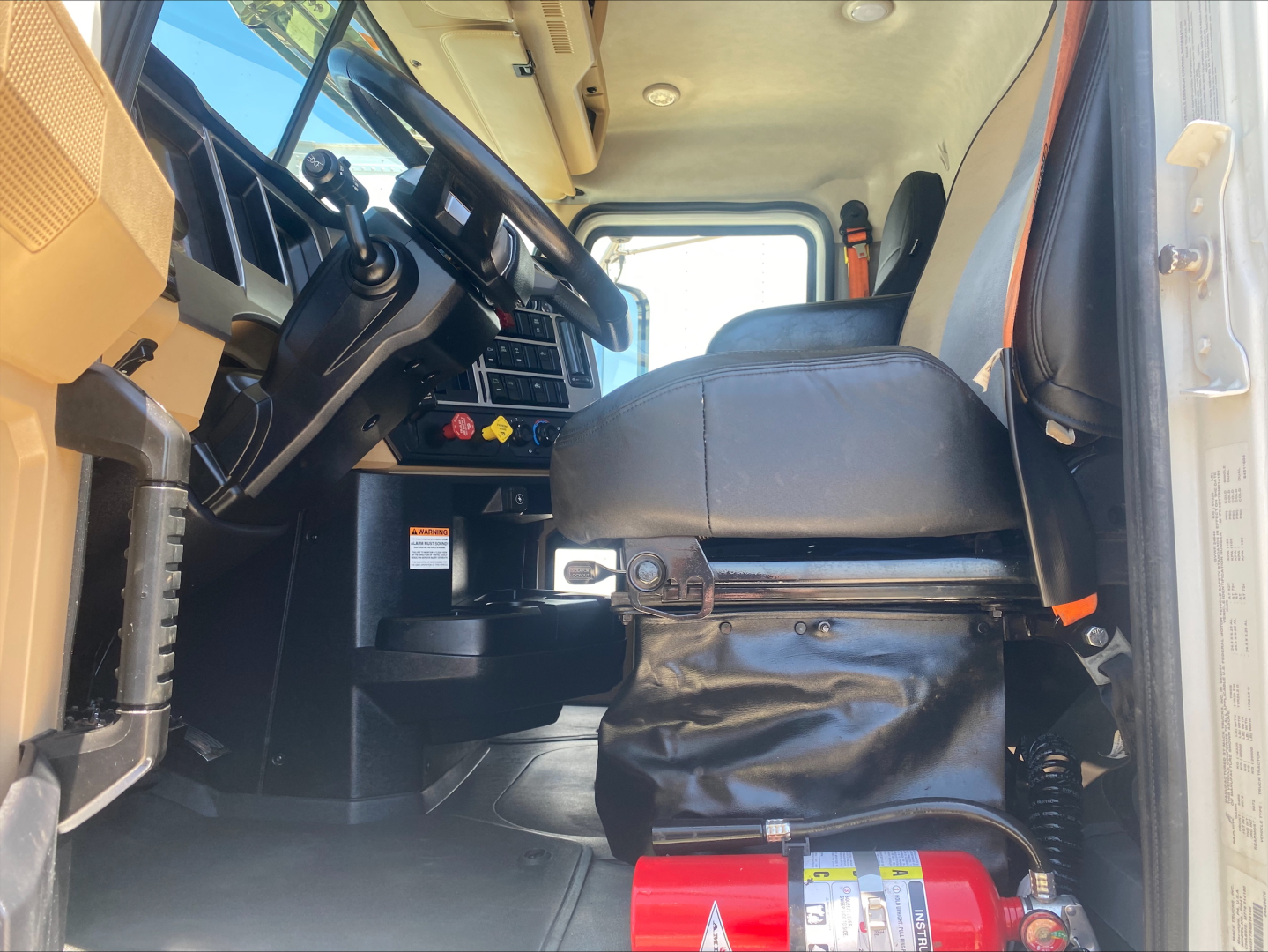 Cab interior of a 2024 Mack PI64T truck showing steering wheel, dashboard, driver seat, and winch controls with a red fire extinguisher at the floor.