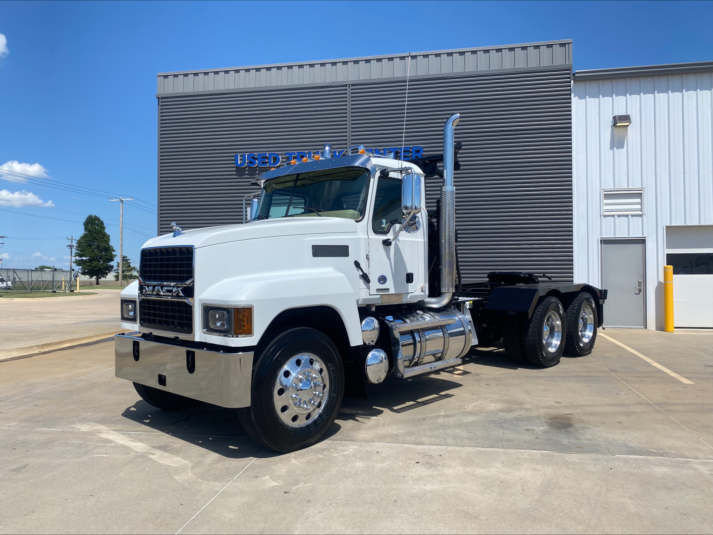 White 2024 Mack PI64T heavy-duty truck with a large black winch body in the bed, chrome front bumper, dual rear axles, and polished wheels, parked outside a service building.