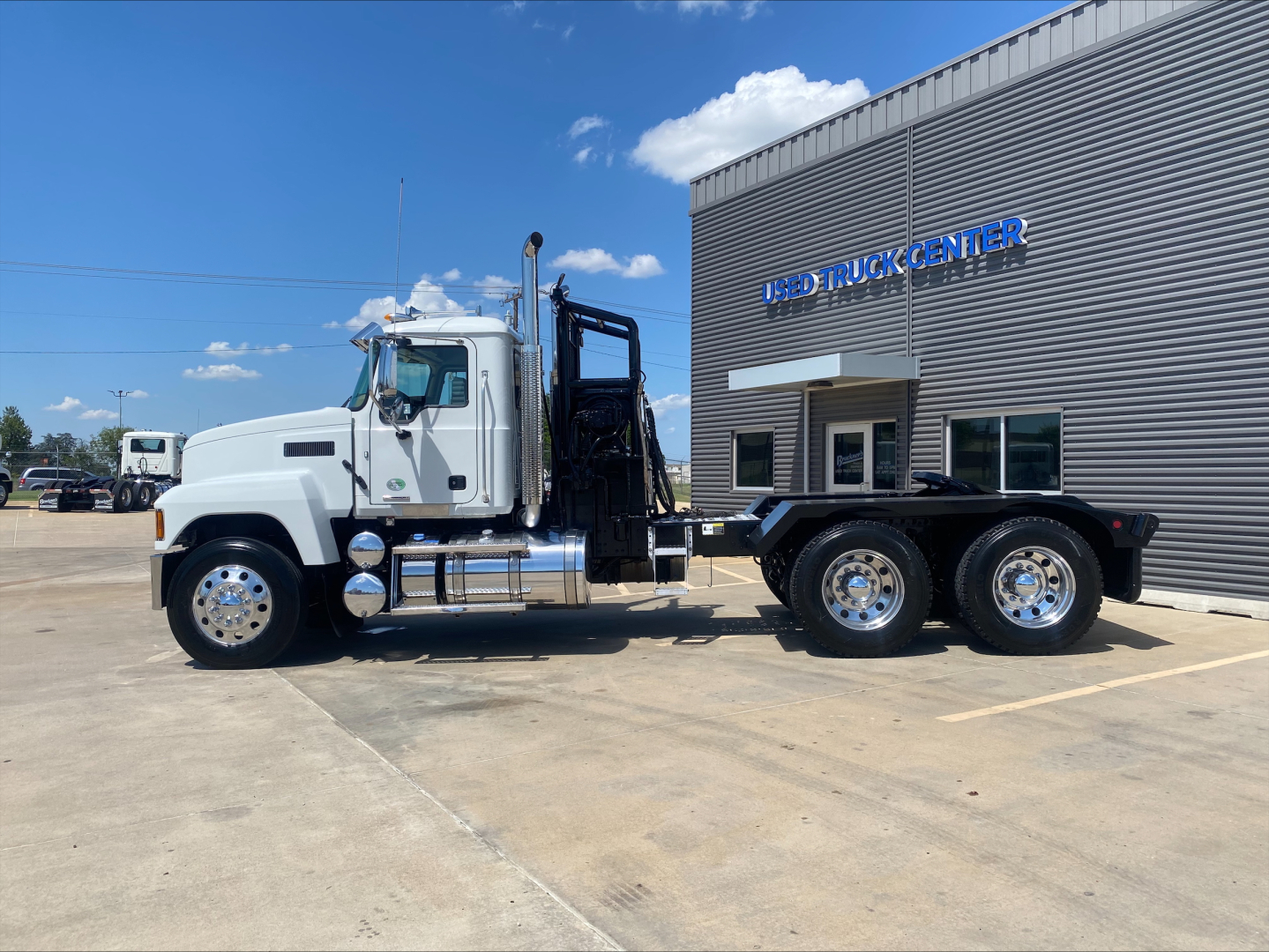 Truck side view of a 2024 Mack PI64T with winch, white cab, black chassis, and dual rear axles in a dealership lot.