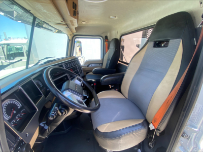 Mack PI64T truck cab interior showing steering wheel dashboard and two-tone seat upholstery with seat belt. Dash gauges visible.