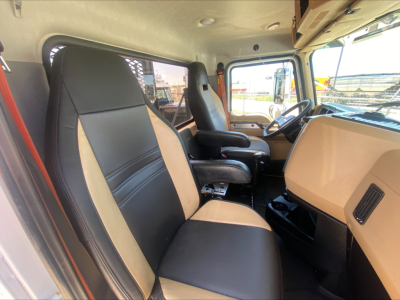 Cab interior of Mack PI64T showing two-tone beige and black front seats, steering wheel, and dashboard from driver side.