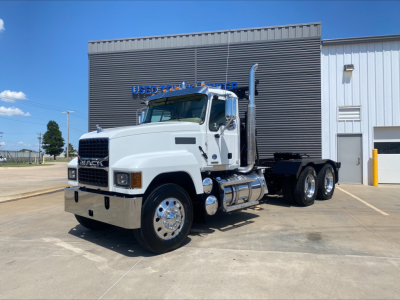 White 2024 Mack PI64T heavy-duty truck with a large black winch body in the bed, chrome front bumper, dual rear axles, and polished wheels, parked outside a service building.