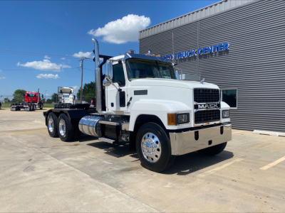 2024 Mack PI64T heavy truck with winch, white cab, chrome fuel tanks, and dual rear axles in front of a building. Visible text includes 'MACK' on the grille and 'TRUCK CENTER' on the building.