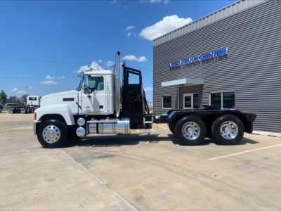 Truck side view of a 2024 Mack PI64T with winch, white cab, black chassis, and dual rear axles in a dealership lot.
