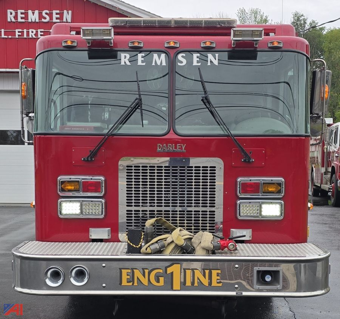 Fire truck front view showing REMSEN lettering on windshield, DARLEY badge, grille, and ENG1NE on bumper; red cab with wavy hoses and chrome bumper.