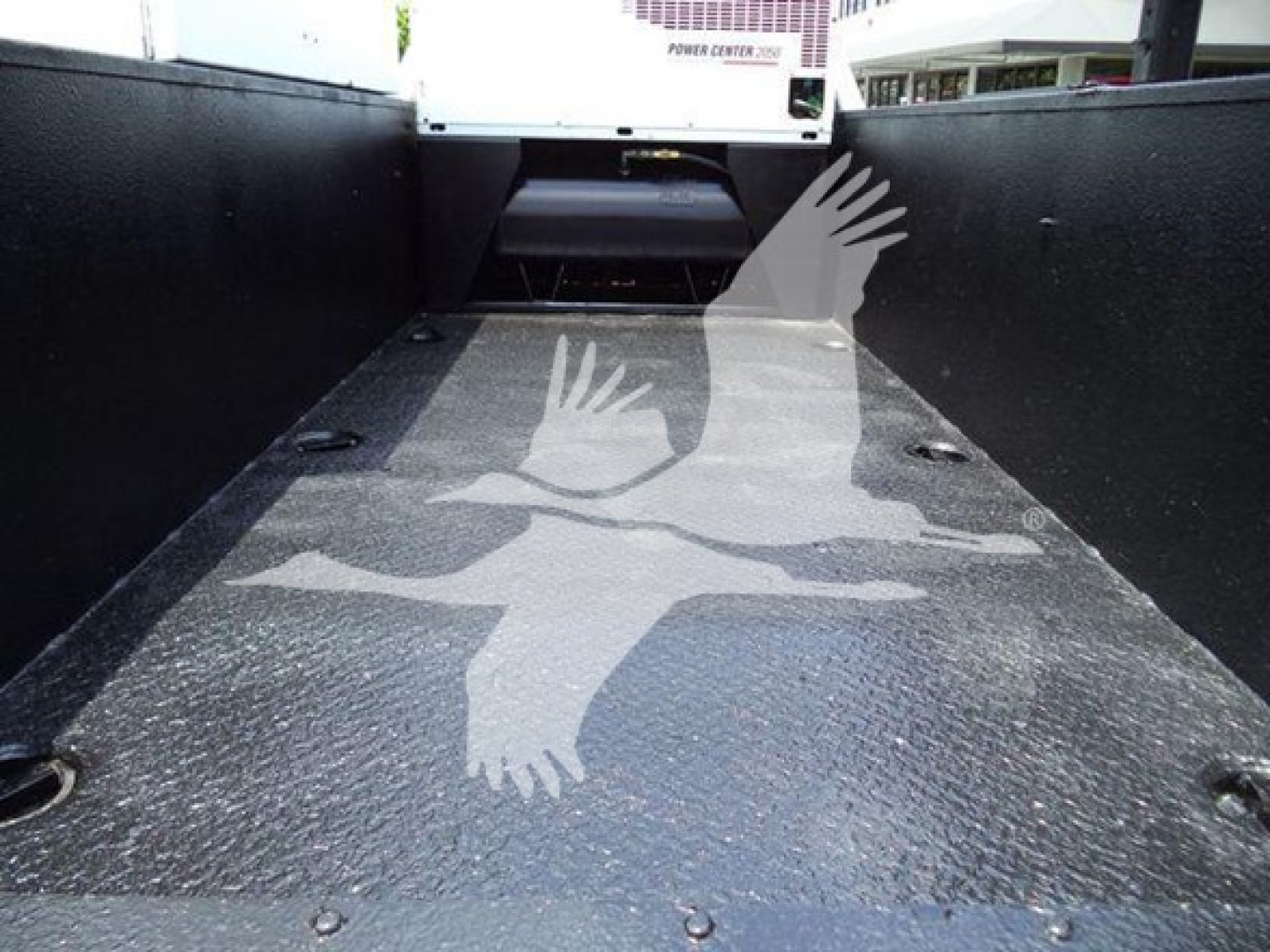 Flatbed truck bed with textured metal surface, Ford rear area visible, seating area appears in background.