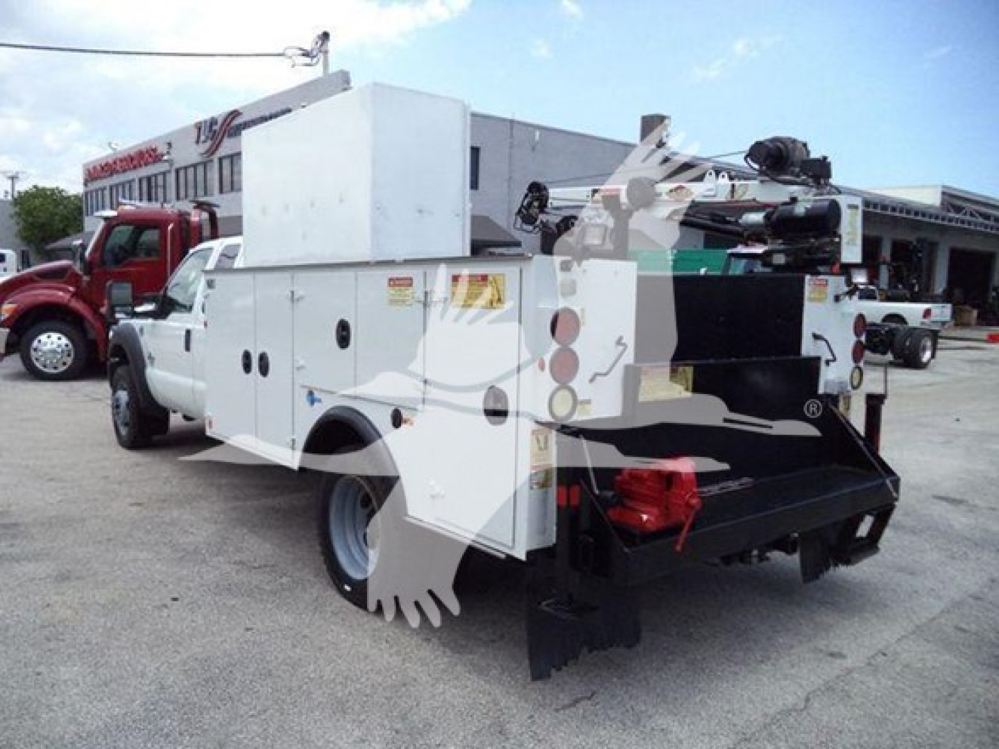 Ford utility truck in service/utility yard with large white service body and equipment rear view showing compartments and a crane attachment.