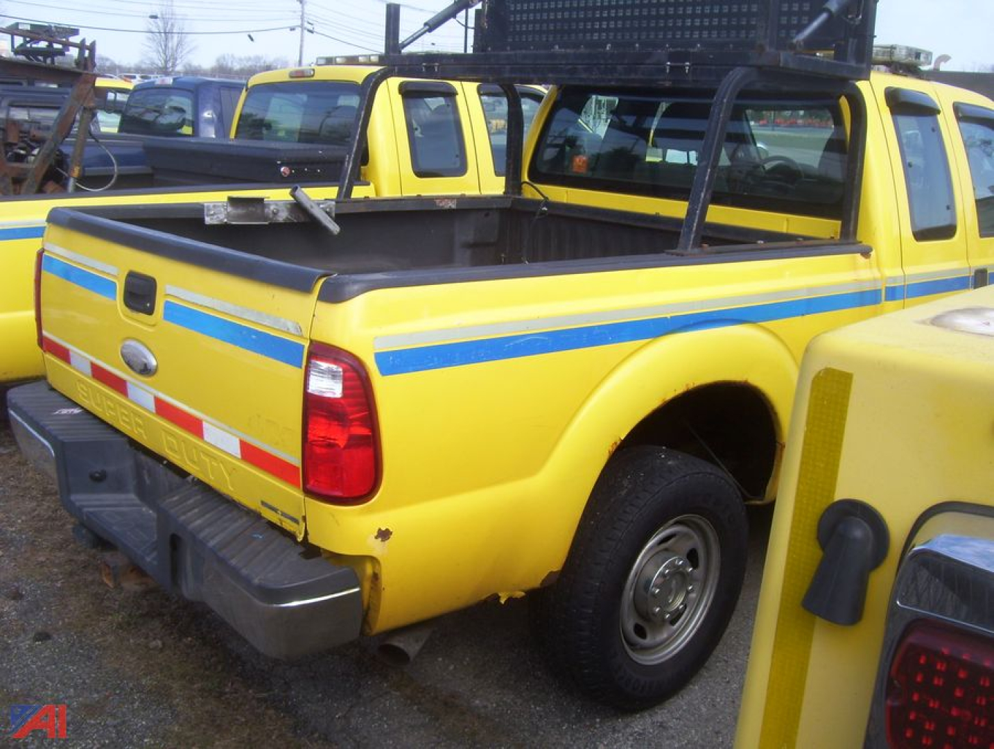 Yellow Ford F-250 Super Duty pickup truck in a lot with blue stripe decals on the bed side and dual rear taillights.